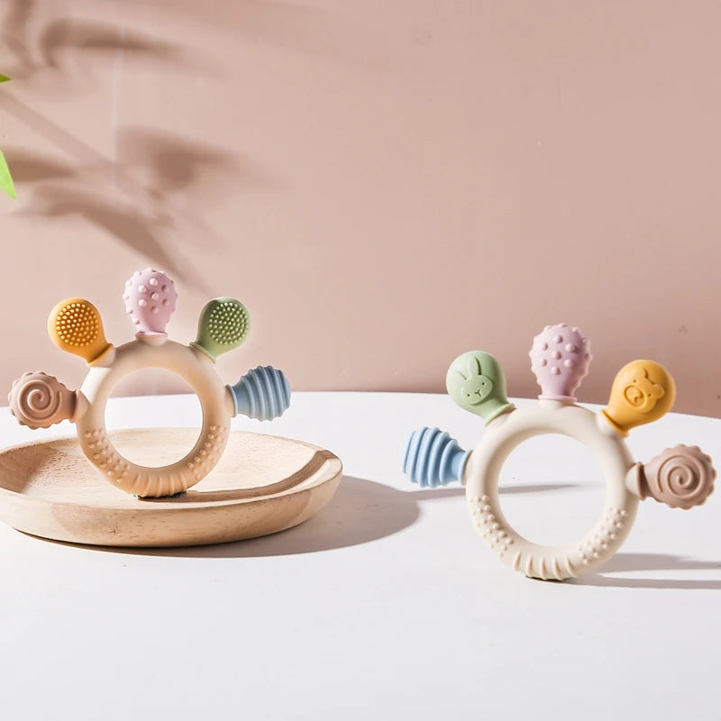 Set aus Silikon-Teether-Ringen in verschiedenen Farben, darunter gelb, rosa und grün, auf einer weißen Oberfläche.