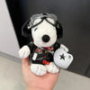 A white plush dog with black ears wearing sunglasses and a red collar is held against a dark background.