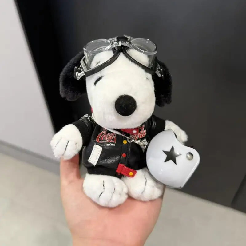 A white plush dog with black ears wearing sunglasses and a red collar is held against a dark background.