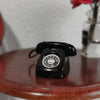 A black vintage rotary telephone miniature resting on a wooden surface.