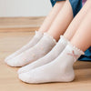 A stack of five white floral cotton kids socks is shown on a wooden surface.