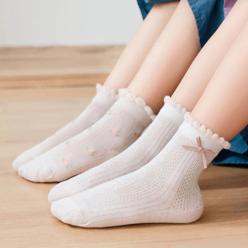 A stack of five white floral cotton kids socks is shown on a wooden surface.