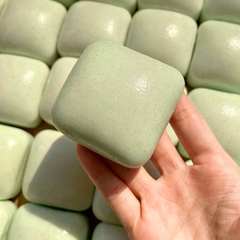 A hand holds a soft, light green sticky cube stress relief toy against a background of similar cubes.