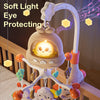 A white musical mobile with a soft light eye protecting feature hangs above a wooden crib railing.