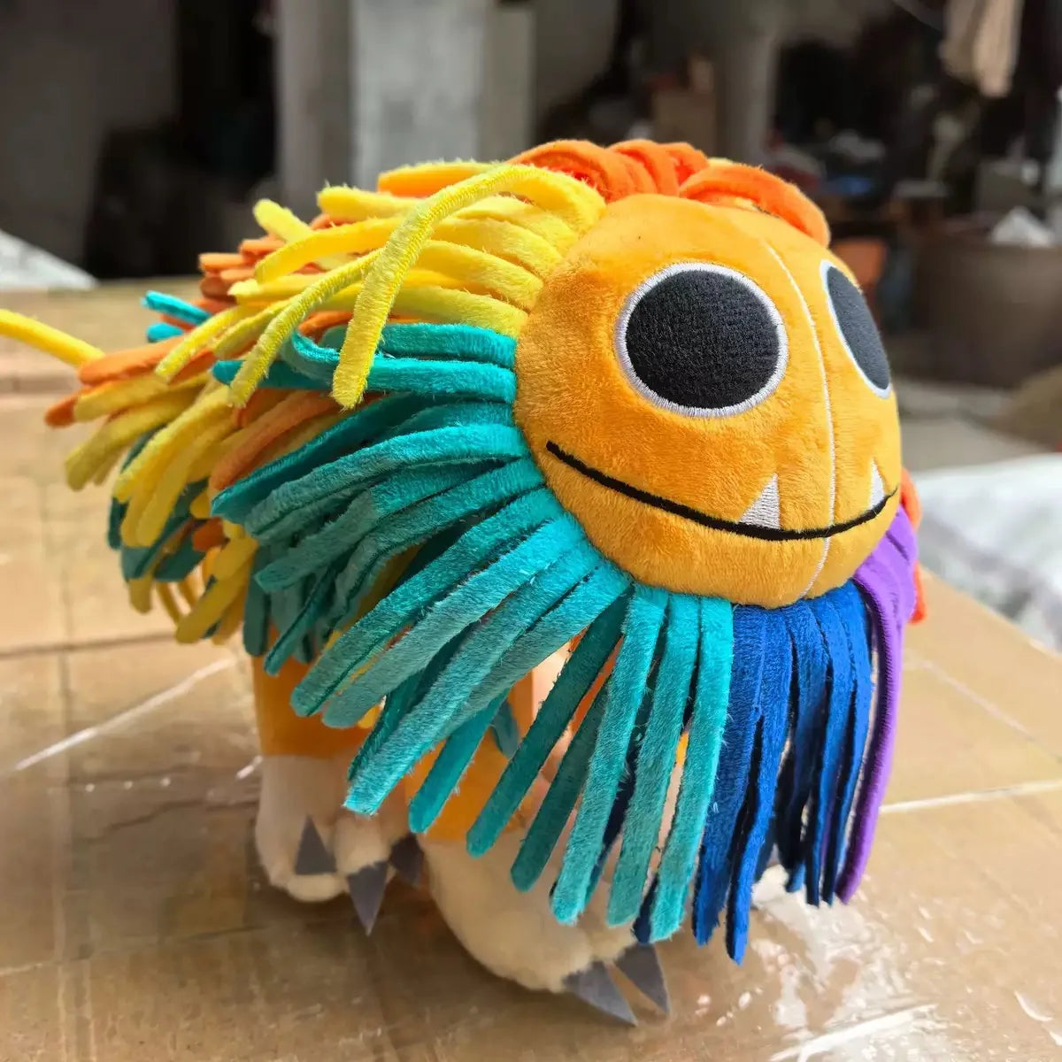 A colorful lion plush toy with bright orange, yellow, and turquoise yarn hair.