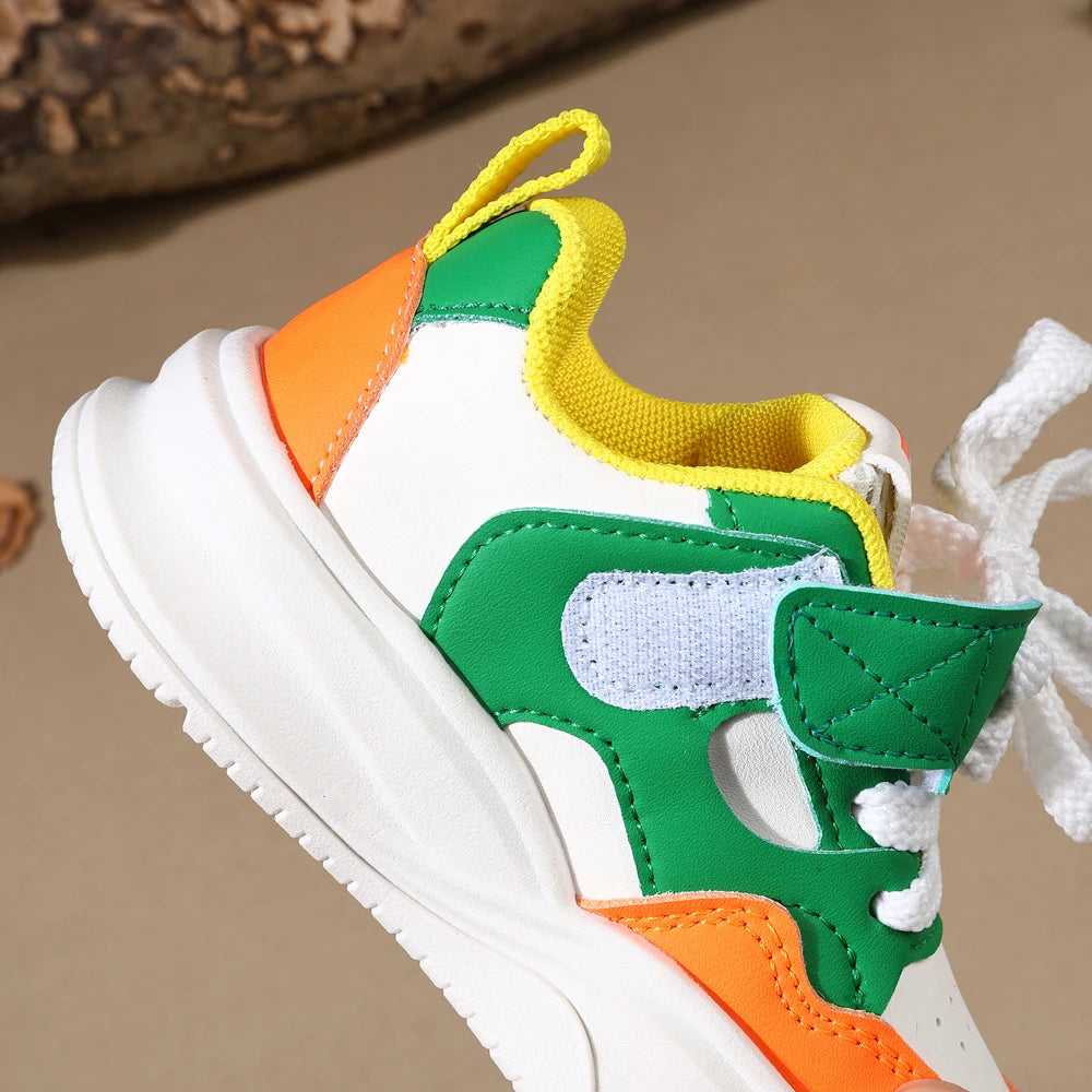A close-up of a white sneaker with hook-and-loop straps in green, orange, and yellow accents.
