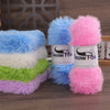 A collection of brightly colored chunky faux fur yarn skeins in blue, pink, and green stacked on a wooden surface.