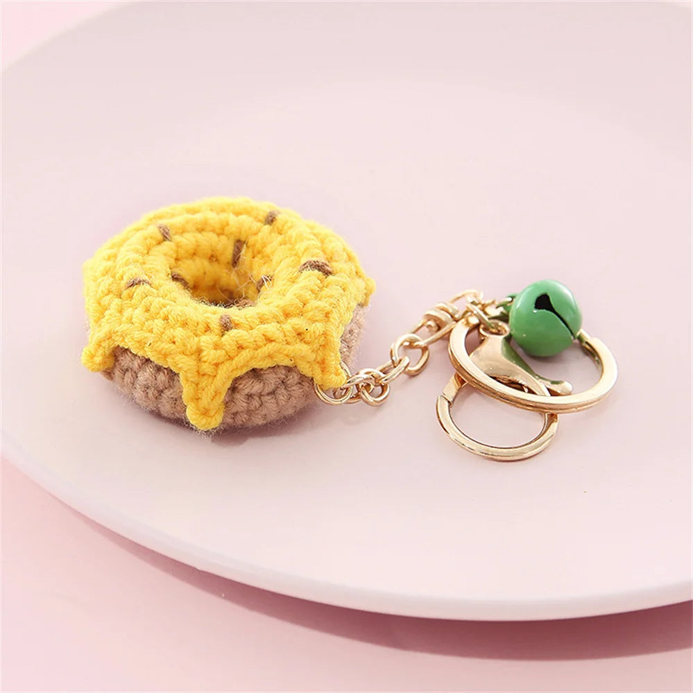 A yellow crochet fruit pendant shaped like a donut rests on a pink plate.