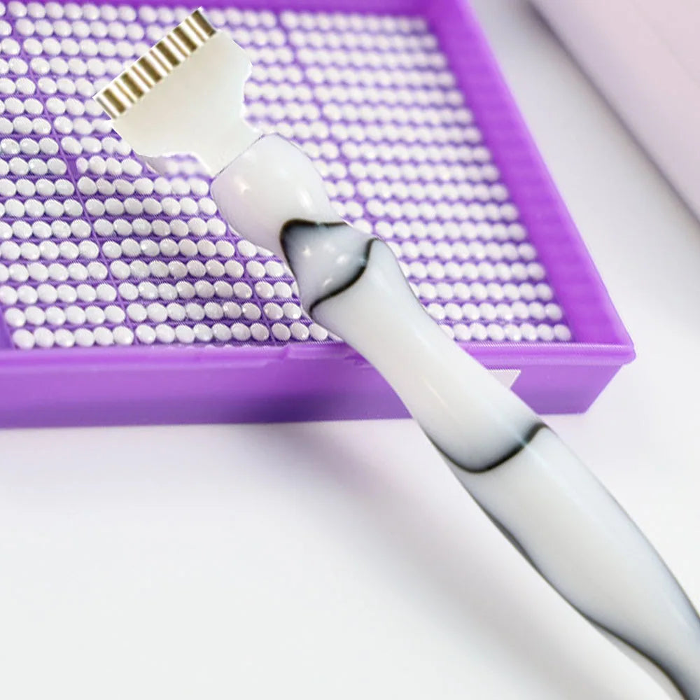 A white diamond painting pen set with interchangeable tips resting in a purple tray.