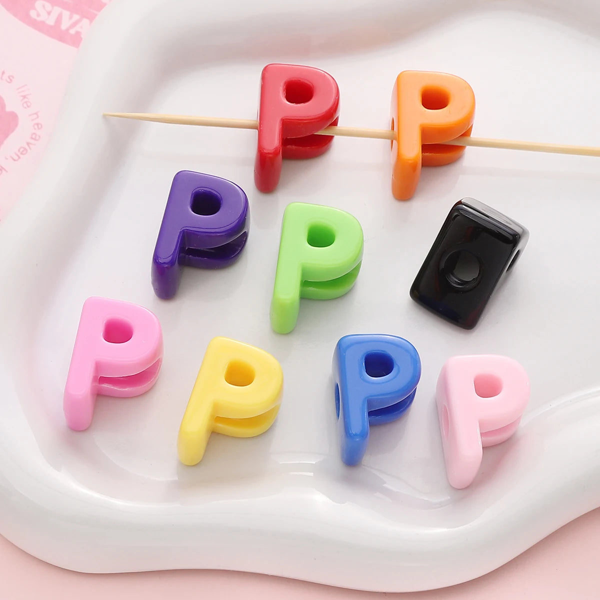 Colorful acrylic letter beads in various colors are arranged on a white tray with wooden sticks.