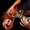 Hands playing an acoustic guitar with decorative picks and a leather keychain holster.