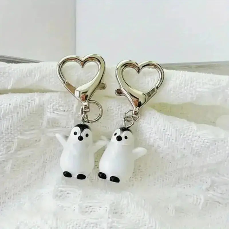 A silver heart keychain set featuring two small white penguin charms