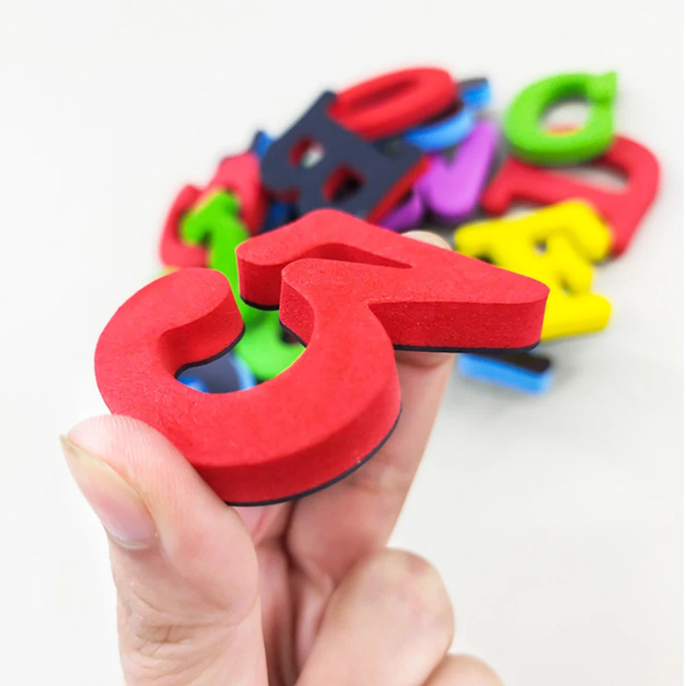 A hand holds a colorful magnetic letter and number set, showing various shapes in red, blue, green, and yellow.