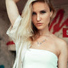A blonde woman wearing a white top and jacket, looking directly at the camera.