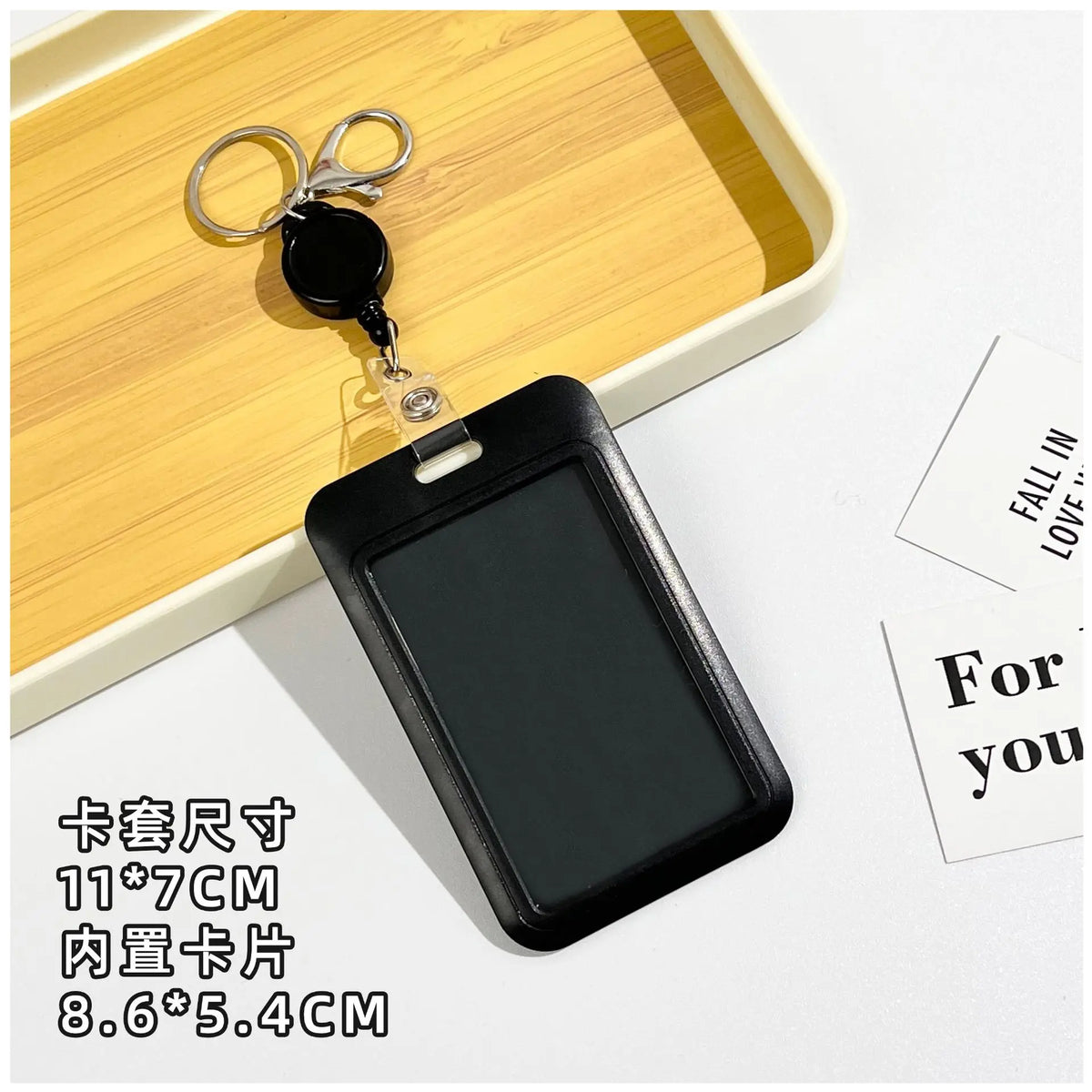 Black rectangular ID badge holder with a keychain attached, shown resting on a wooden tray.