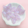 A collection of iridescent pink and purple mermaid bowknot beads displayed on a white dish.