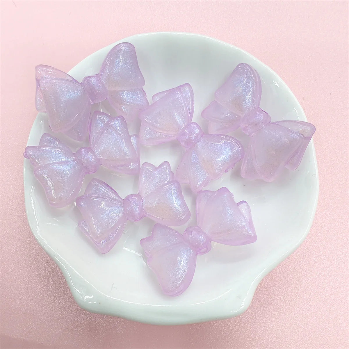 A collection of iridescent pink and purple mermaid bowknot beads displayed on a white dish.