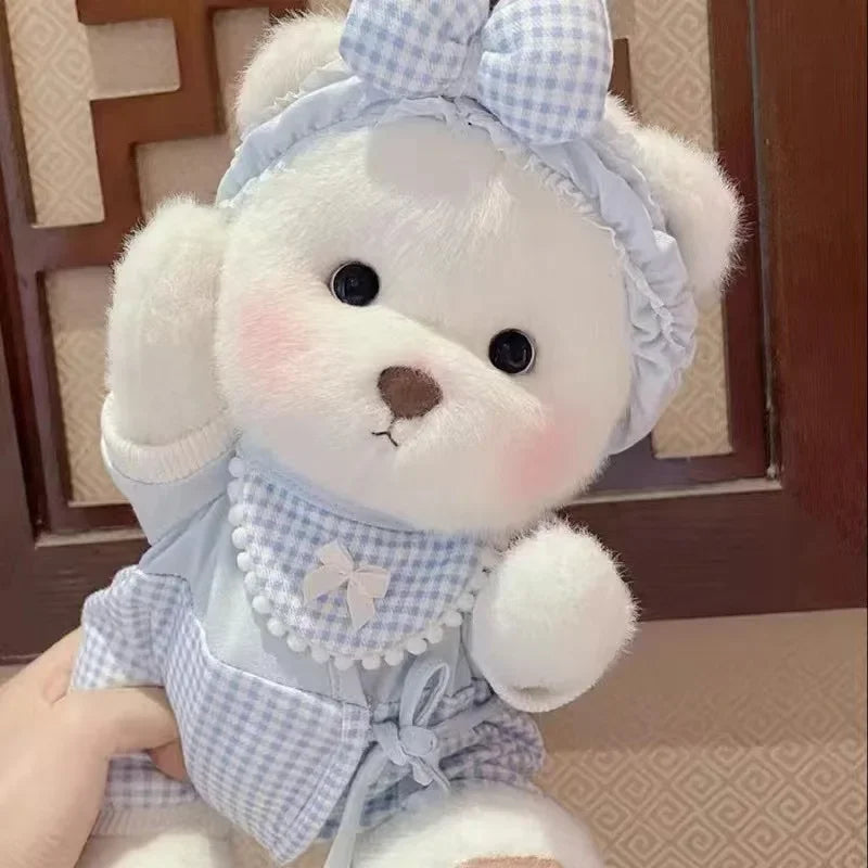 A white teddy bear plush wearing a light blue checkered dress and matching bow