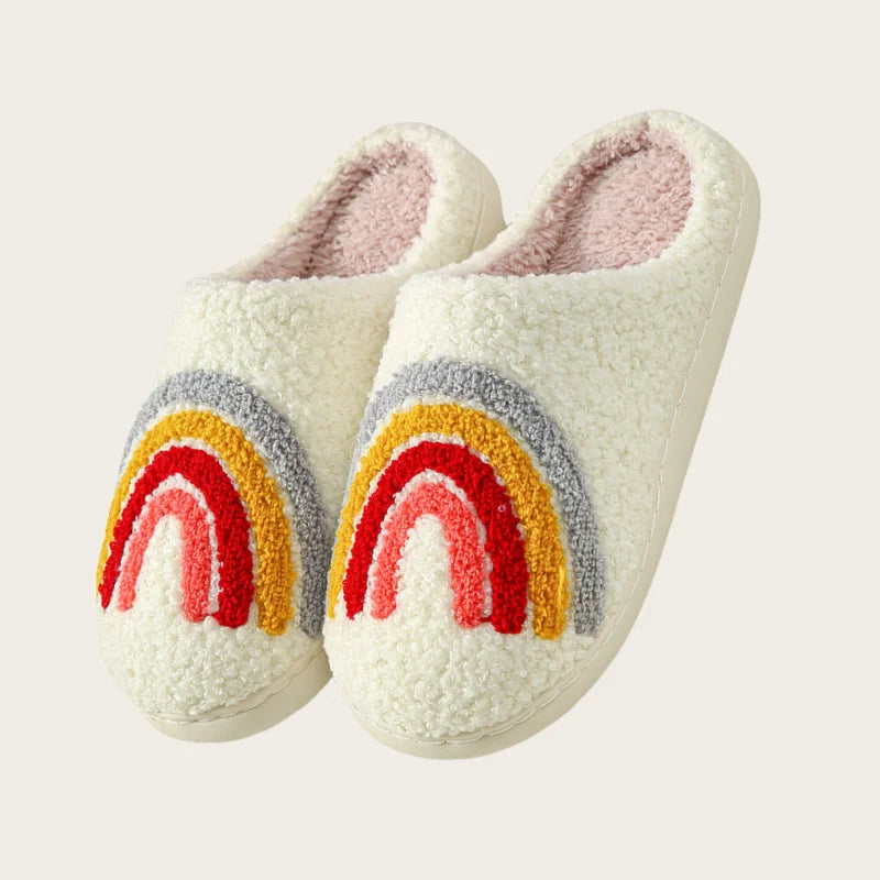 A pair of white plush indoor slippers decorated with a rainbow design in red, yellow, and gray.