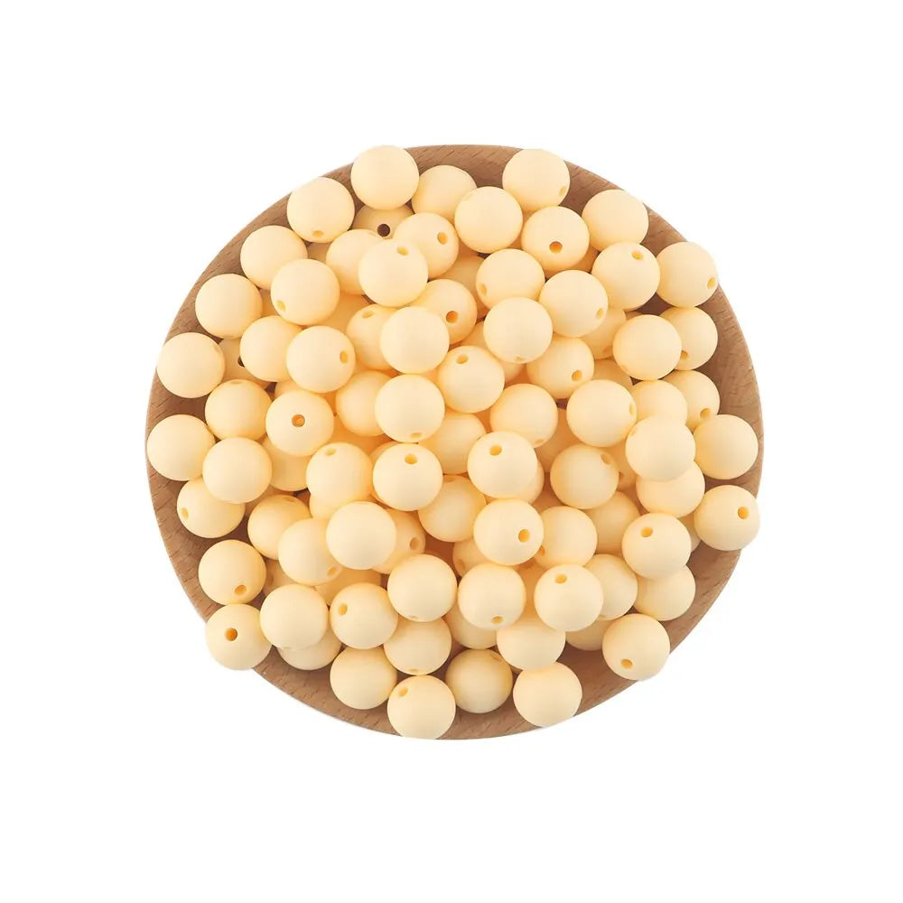 A pile of small, pale yellow silicone round beads for jewelry making and DIY crafts resting on a wooden surface.