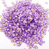 A pile of small purple polymer clay flower charms with yellow centers for DIY crafts