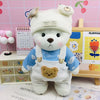A white plush doll wearing a blue outfit with white overalls and a yellow face patch, displayed on a wooden surface.