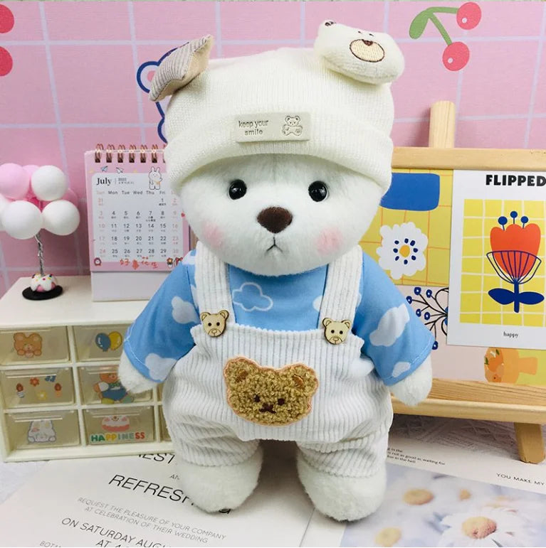 A white plush doll wearing a blue outfit with white overalls and a yellow face patch, displayed on a wooden surface.