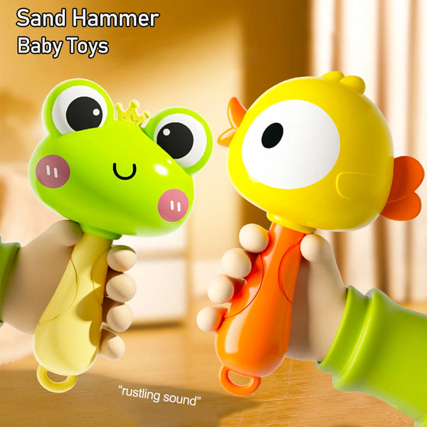 A hand is holding a yellow sand hammer baby toy shaped like a frog, demonstrating a rustling sound.