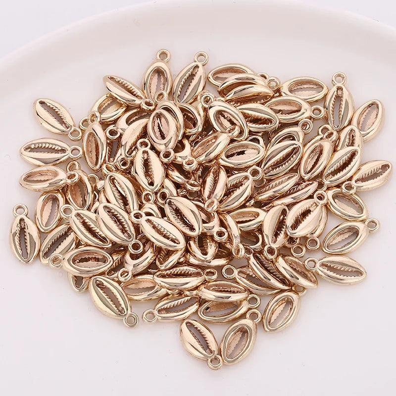 A pile of 50 small, gold-colored plastic seashell charms for jewelry making.