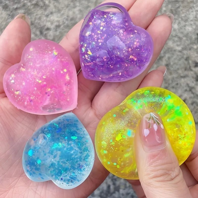 A hand holds three heart-shaped squishy toys in pink, purple, and blue colors.