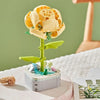 A small building block set shaped like a yellow rose flower with green leaves on a white base.