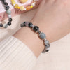 A wrist wearing a bracelet made of various colored glass beads including black, gray, and amber stones.