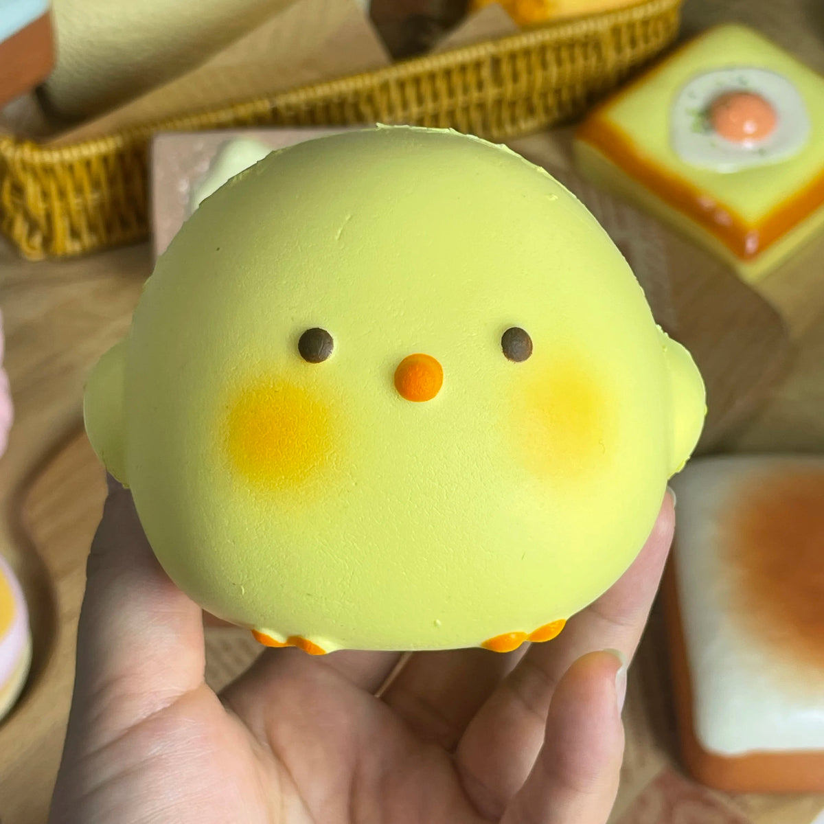 A hand holds a yellow squishy toy shaped like a chick with orange beak and eyes.