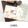 A vintage craft oil-based ink pad featuring an orange butterfly design on a white card, set against a dark wooden background.