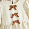 A cream-colored girls' long sleeve dress with three brown fabric bows on the chest.