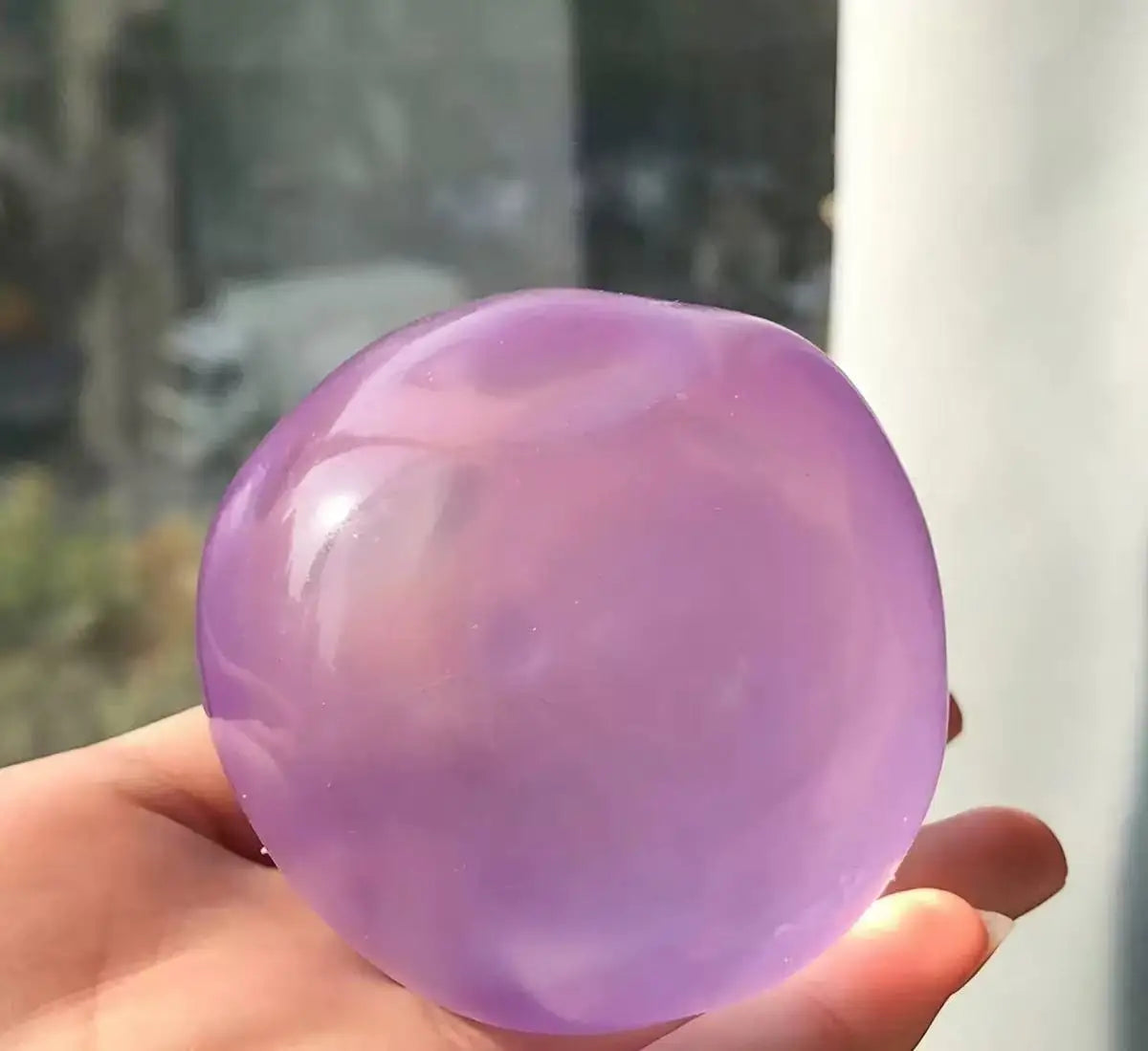 A hand holds a smooth, translucent lavender stress ball made of resin.