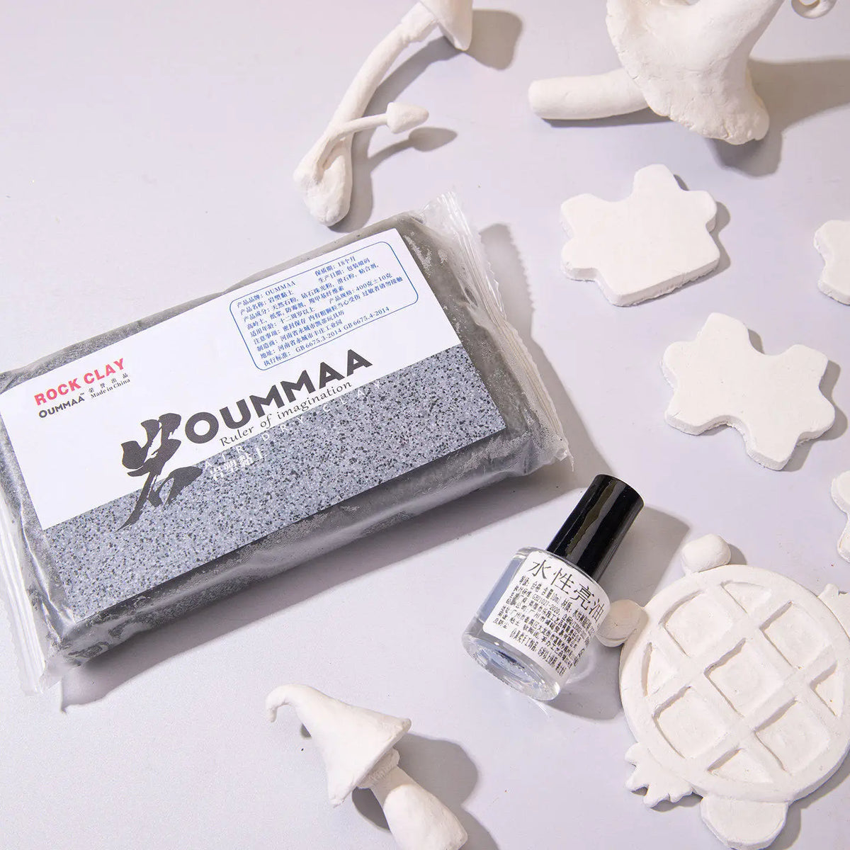 A package of OUMMAA rock clay modeling clay next to several white sculpted clay shapes.