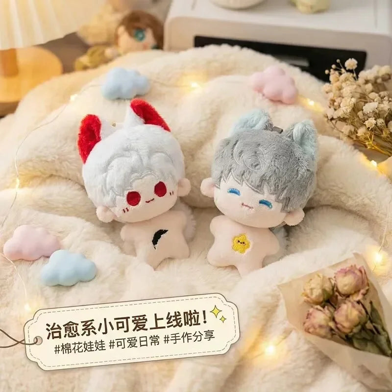 A pair of cute anime plush keychains with pink and blue hair resting on a fluffy white blanket.