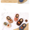 A collection of cozy plush baby slippers in various colors including blue, brown, and pink, shown on a woven mat.