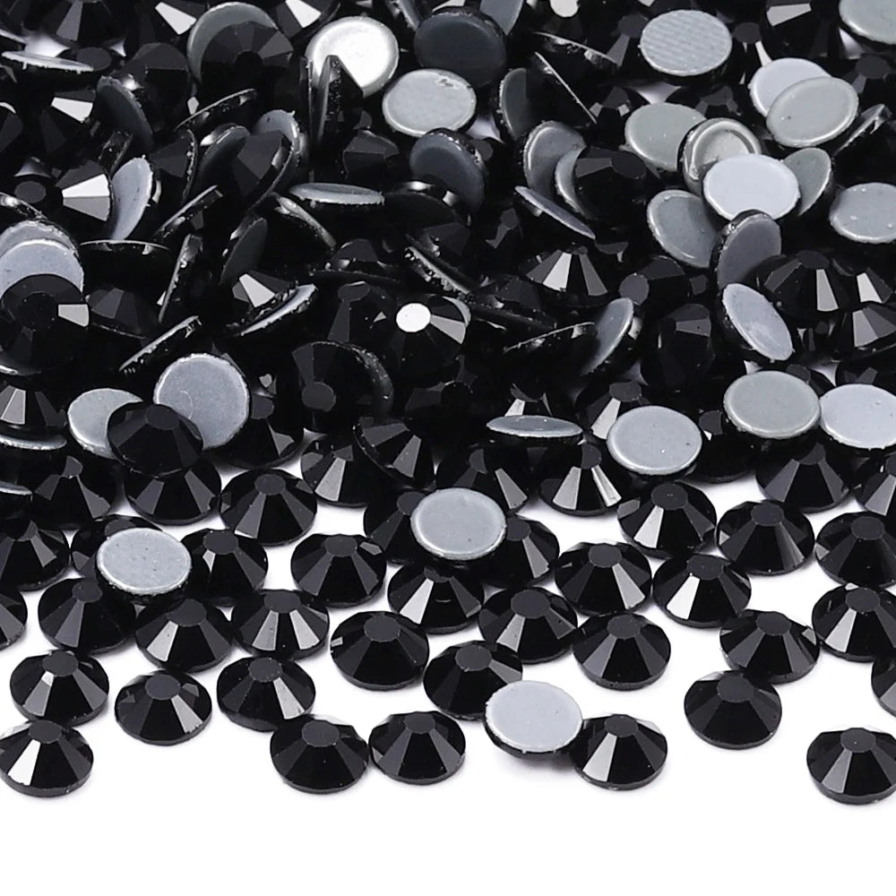 A close-up view of black glass crystal hot fix rhinestones scattered on a white background.