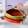An orange Alpaca themed travel storage bag with three zippered compartments is being held open on a white surface.