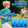 A boy is holding and firing a blue electric water gun outdoors during a summer water game.