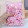 A hand holds a clear bag filled with pink and iridescent 3D resin nail charms for crafting.