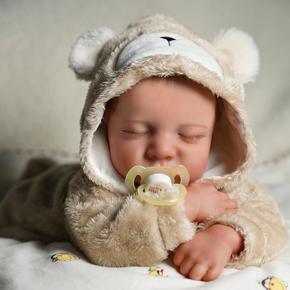A realistic vinyl reborn baby doll wearing a fluffy bear outfit, sleeping peacefully.