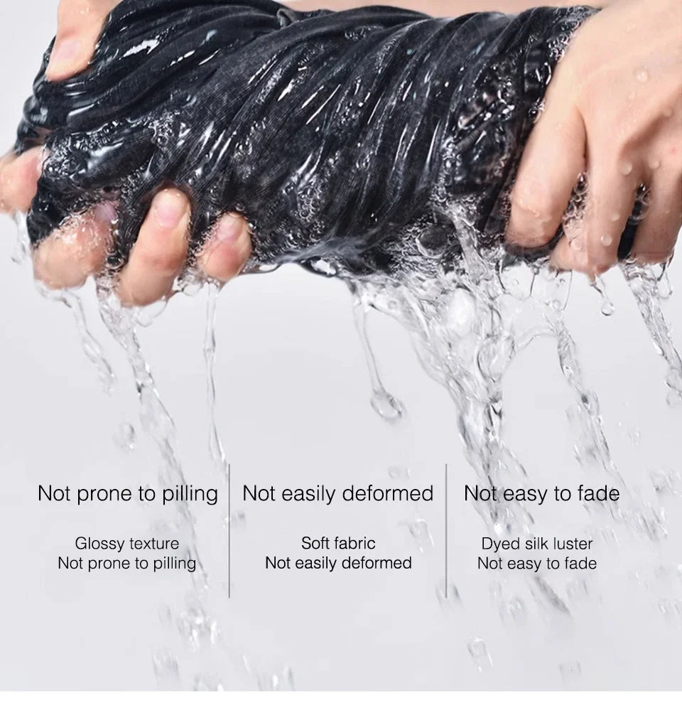 A hand is holding a black, twisted fabric, demonstrating its smooth texture and durability while water flows over it.