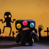 A dark plush monster doll with colorful teeth and eyes sitting on a dark surface.