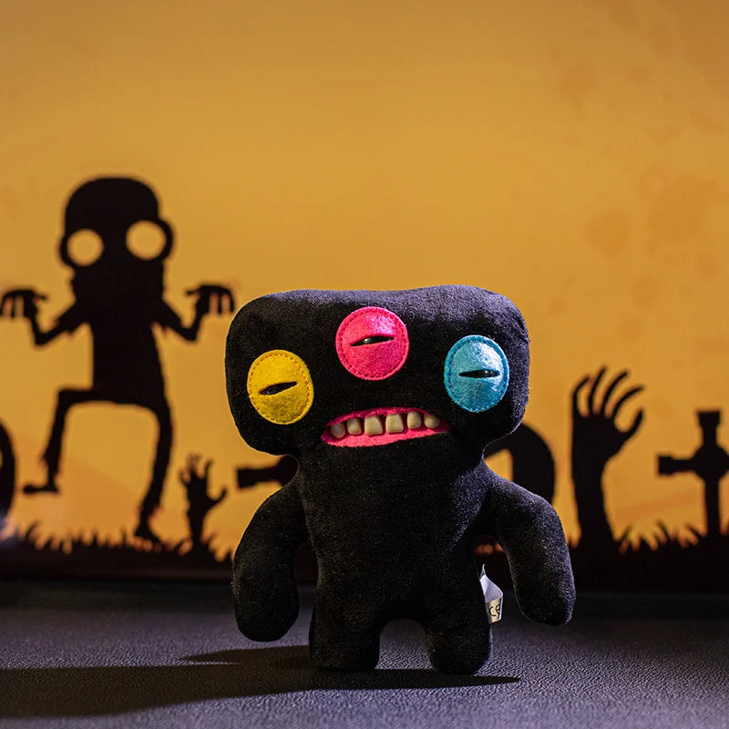 A dark plush monster doll with colorful teeth and eyes sitting on a dark surface.