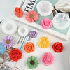 A collection of four silicone flower molds in various shades of pink, orange, and yellow are displayed on a book.