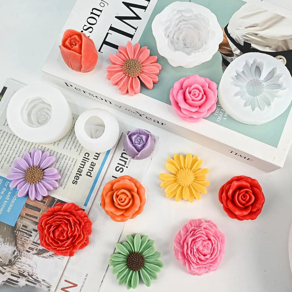 A collection of four silicone flower molds in various shades of pink, orange, and yellow are displayed on a book.