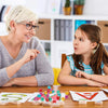 A woman and a girl play with a set of acrylic 6-sided dice on a wooden table.